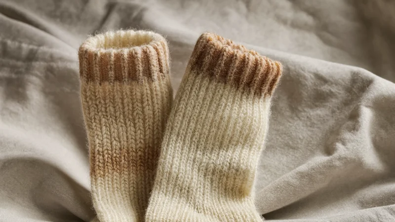 Chaussettes de lit en laine écrue au revers côtelé sur un drap de lin froissé