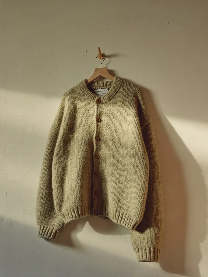 Cardigan en maille gris-vert aux boutons de bois suspendu à une patère murale
