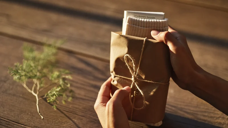 Mains emballant des chaussettes dans du papier kraft uni et de la ficelle naturelle